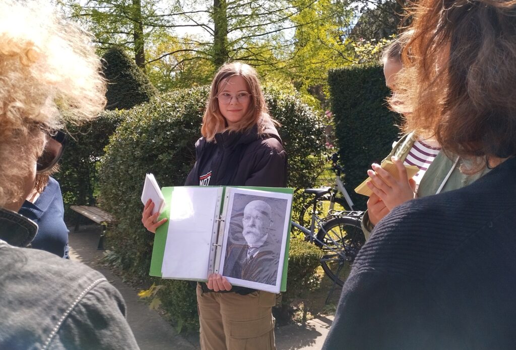Eine junge Frau hält ein Bild von Otto Snell. Sie blickt zu einer Gruppe Menschen.